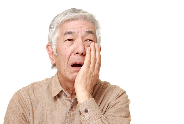 痛そうに頬を押さえている高齢男性